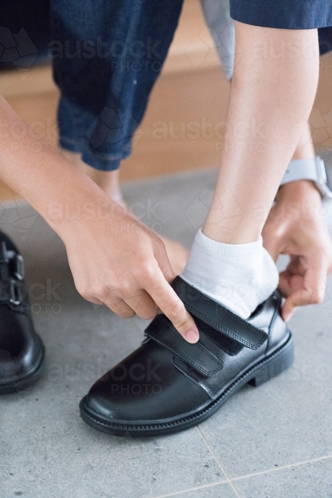 Mother helps her son put on his new school shoes for his first day of school - Australian Stock Image