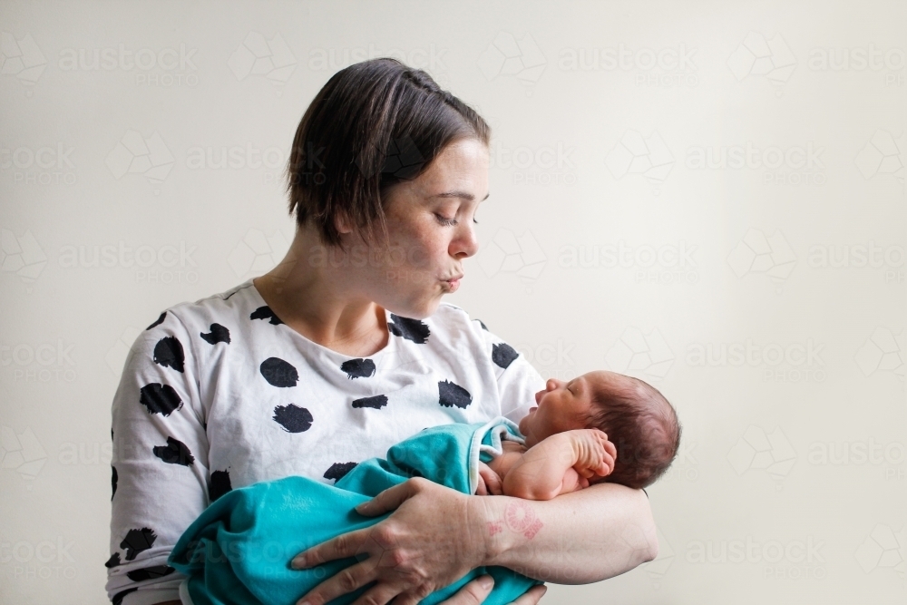 Mother holding her newborn, blowing a kiss to him - Australian Stock Image