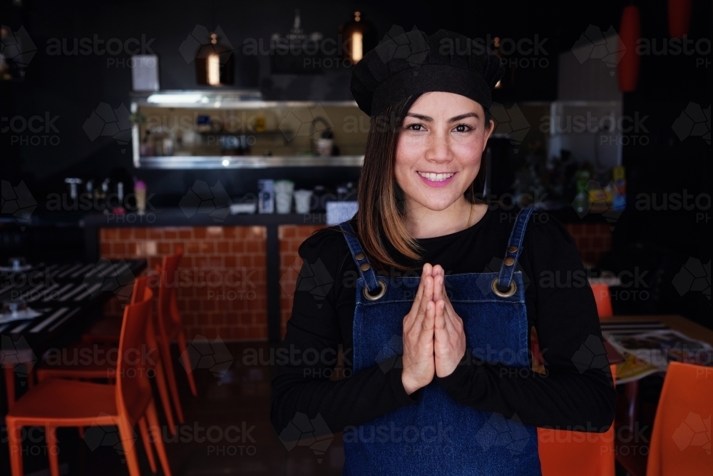 Multicultural Asian small business owner greeting in front of Thai restaurant - Australian Stock Image