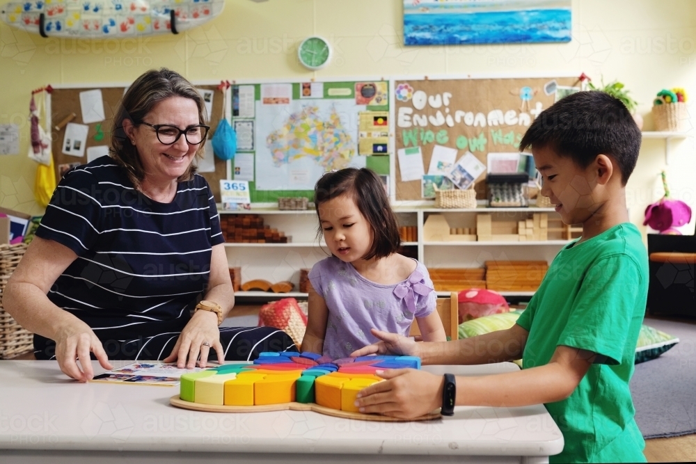 Multicultural teacher and children playing wooden blocks puzzles in kindergarten - Australian Stock Image