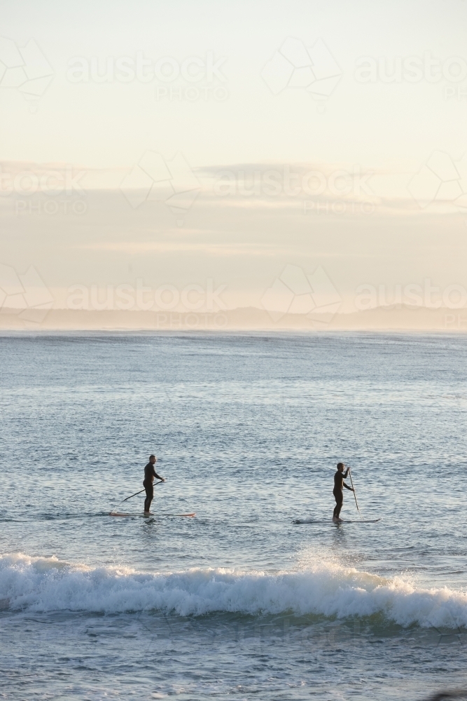 Paddle boarders on ocean at sunrise - Australian Stock Image