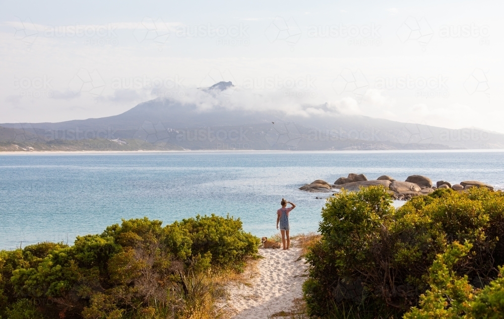 person in landscape looking across Bettys Beach to Mount Manypeaks - Australian Stock Image