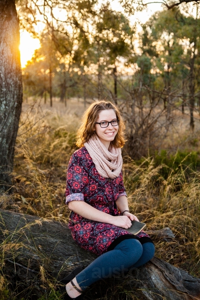 Seventeen year old girl with notebook sitting on log outside - Australian Stock Image