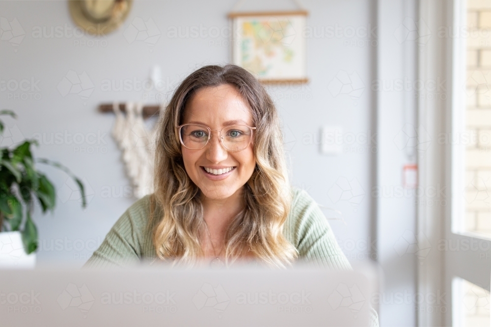 Smiling woman with green blouse wearing an eyeglass while looking at a laptop screen - Australian Stock Image