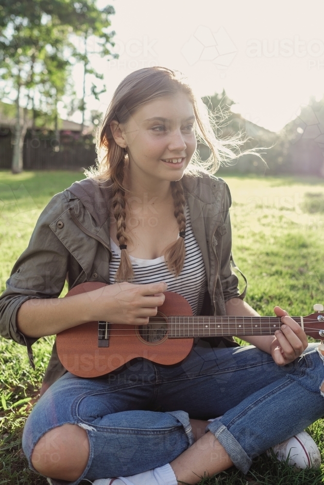 Teenage girl playing ukulele in the park - Australian Stock Image
