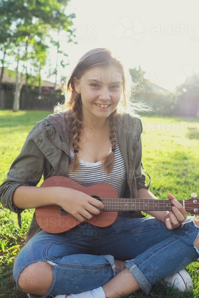 Teenage girl playing ukulele in the park - Australian Stock Image