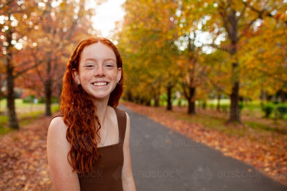 Teenage girl standing in a street lined with Autumn trees - Australian Stock Image