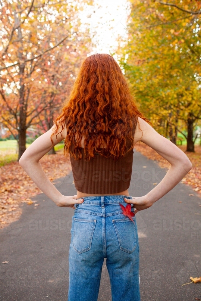 Teenage girl standing in a street lined with Autumn trees - Australian Stock Image