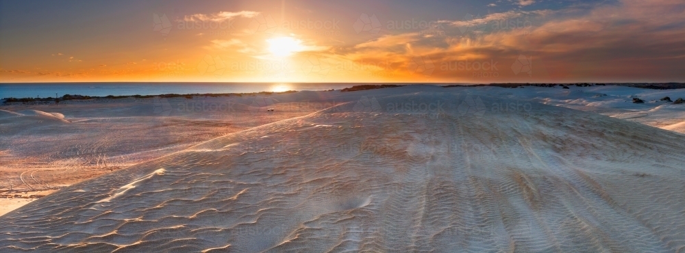 The Sun setting over windswept sand dunes near the coast - Australian Stock Image