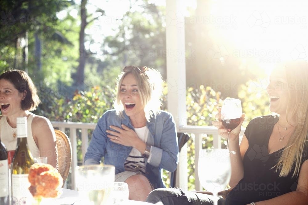 Three laughing women sitting on verandah having drinks - Australian Stock Image