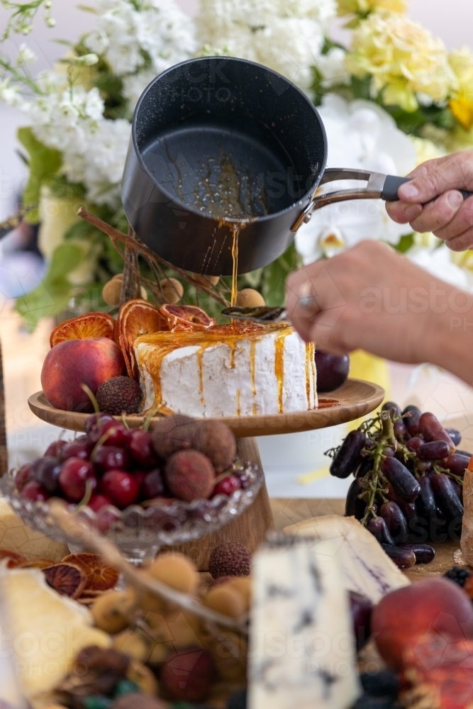 toffee being poured over cheese on platter filled with cheese and fruit - Australian Stock Image