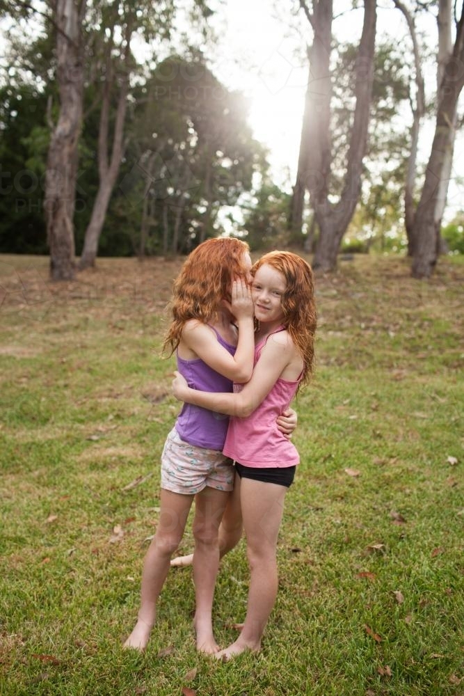 Two girls hugging and telling secrets in a field - Australian Stock Image