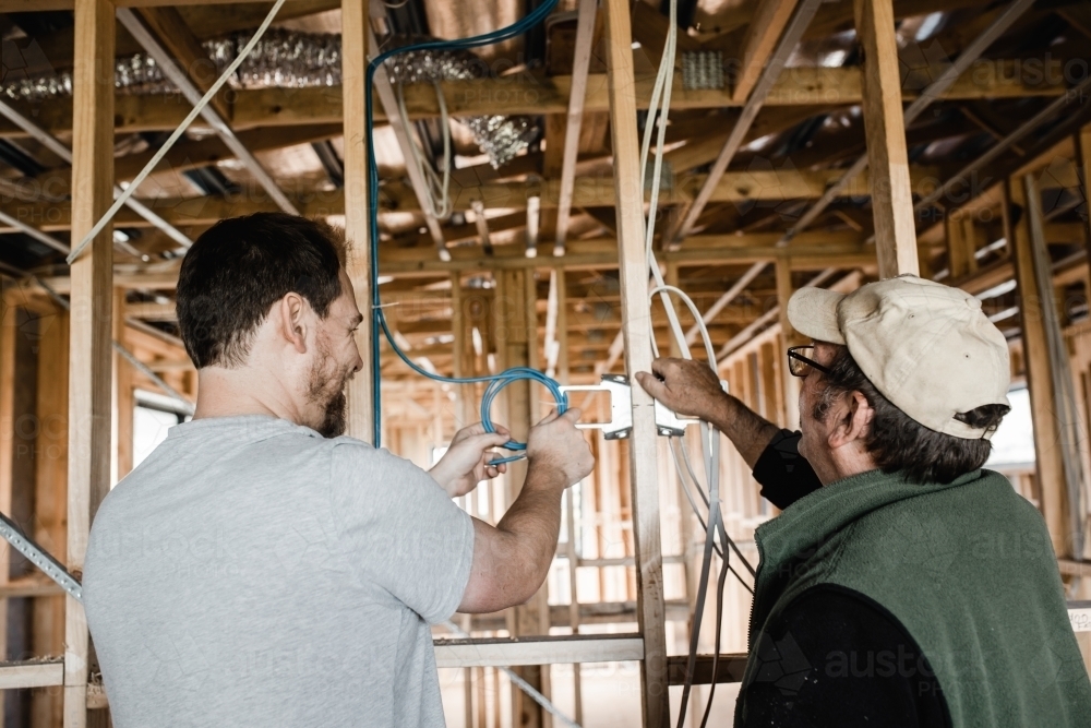 two men are laying cables in a house at frame stage - Australian Stock Image