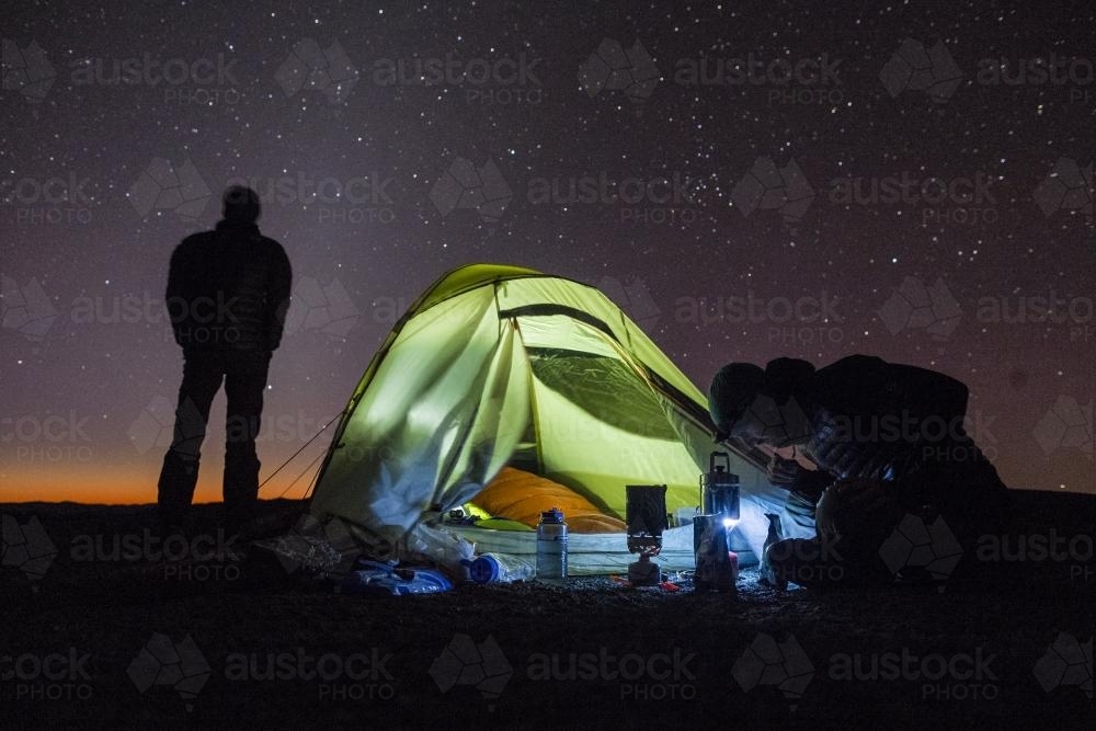 Two men silhouetted with tent camping under the stars - Australian Stock Image