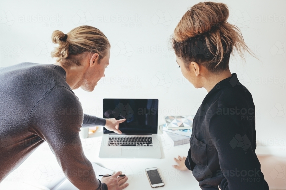 Two office workers looking at a laptop screen together - Australian Stock Image