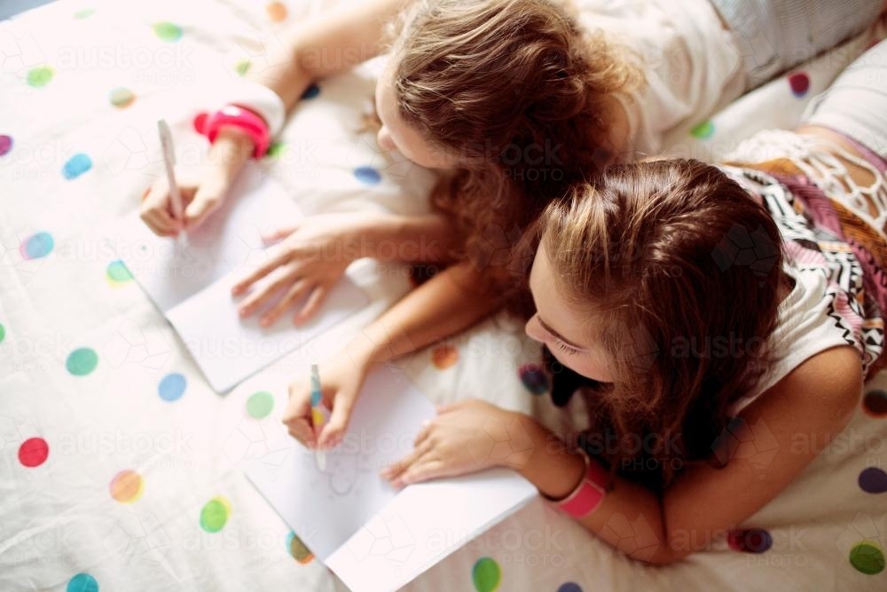 Two young girls writing on a bed - Australian Stock Image