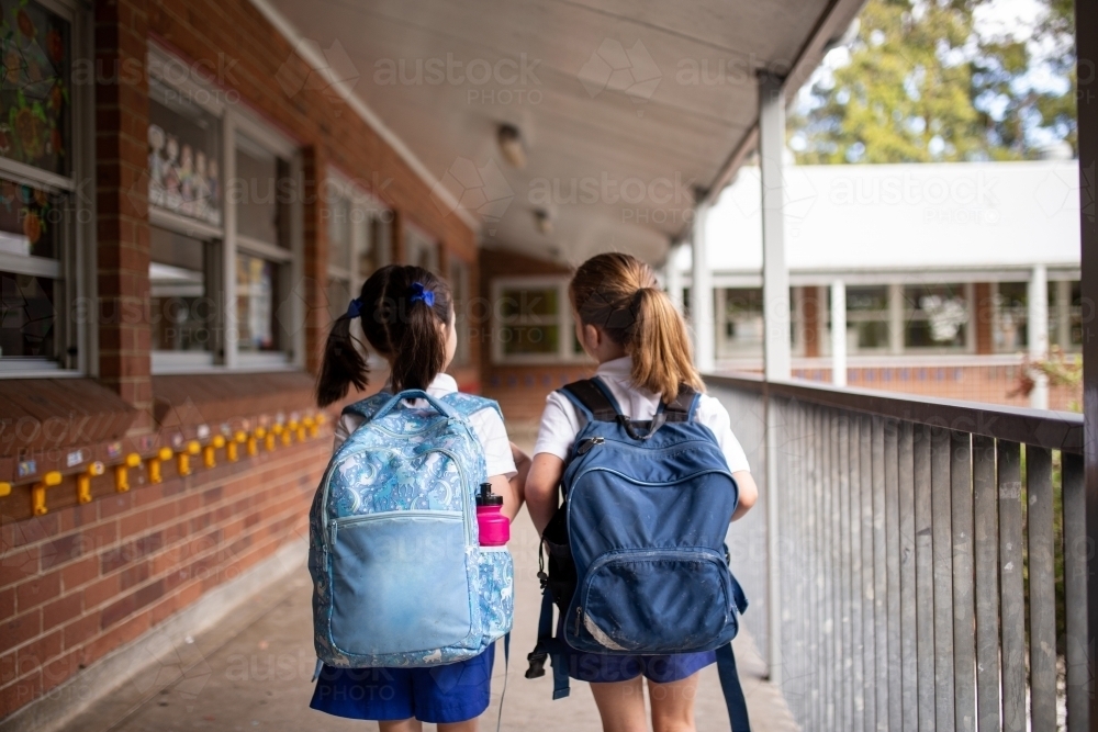 Two young schoolgirls walking along outdoor hallway - Australian Stock Image