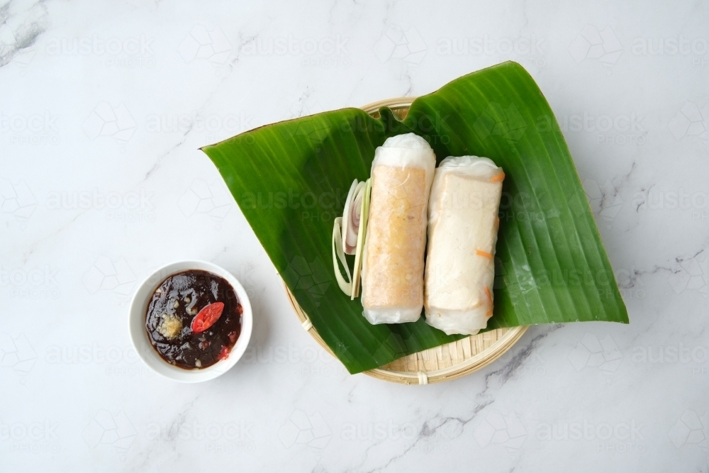 Vietnamese spring rolls on leaf in bamboo bowl with dipping sauce - Australian Stock Image
