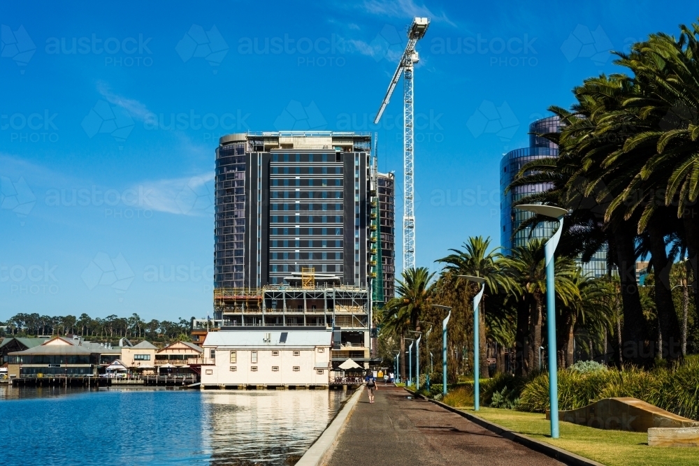 View of buildings and large crane from pathway beside water - Australian Stock Image
