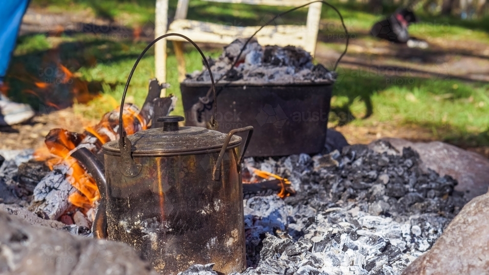 Water billy can and camp oven over hot coals - Australian Stock Image