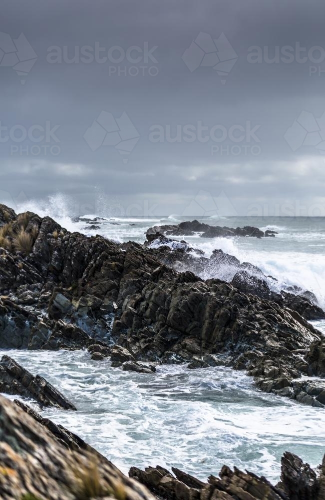 Waves crashing into jagged rocks. - Australian Stock Image