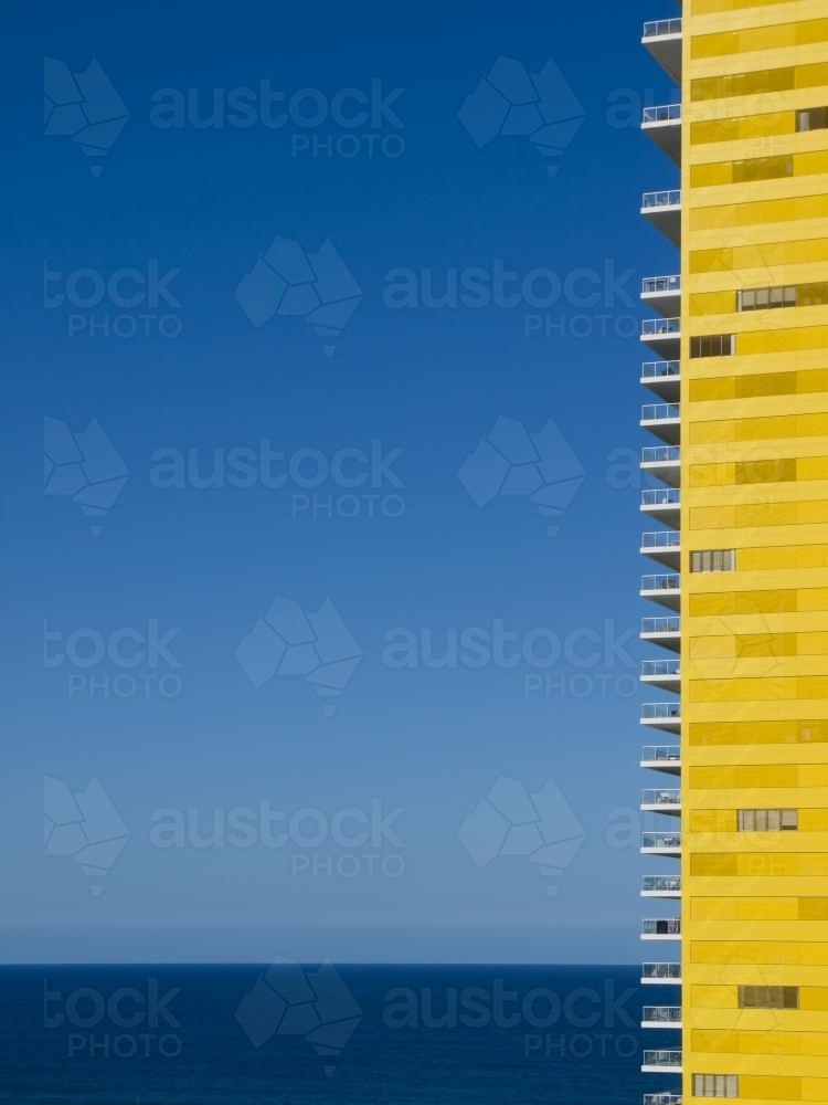 Yellow apartment building with blue sky and sea - Australian Stock Image