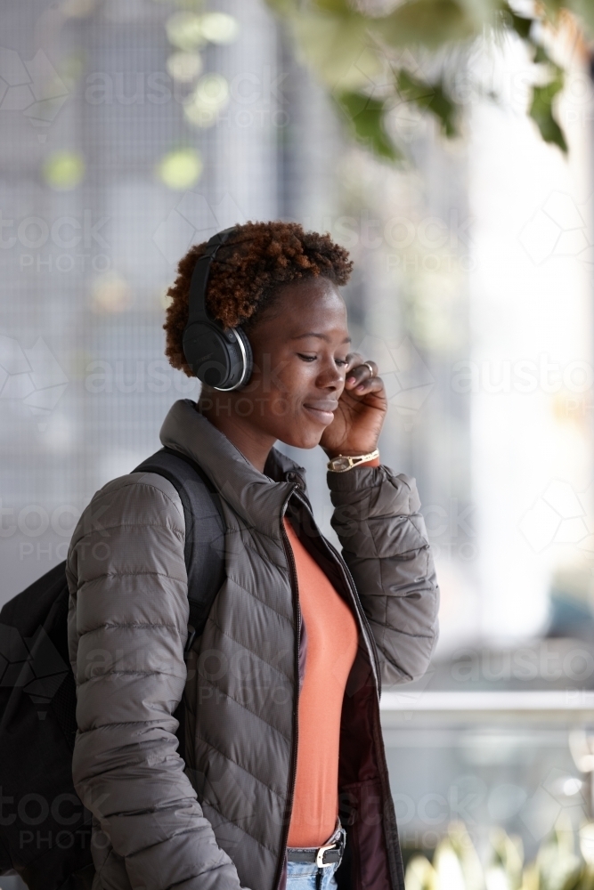 Young African woman listening to music wearing wireless headphones in city - Australian Stock Image