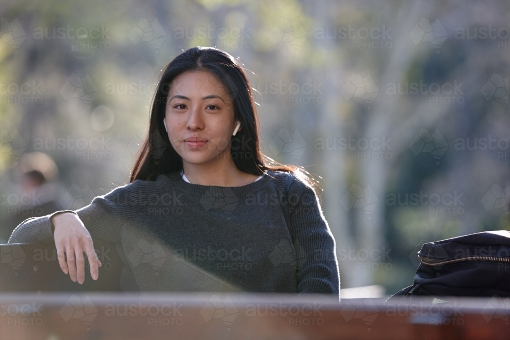 Young Asian female university student listening to wireless headphones outdoors - Australian Stock Image