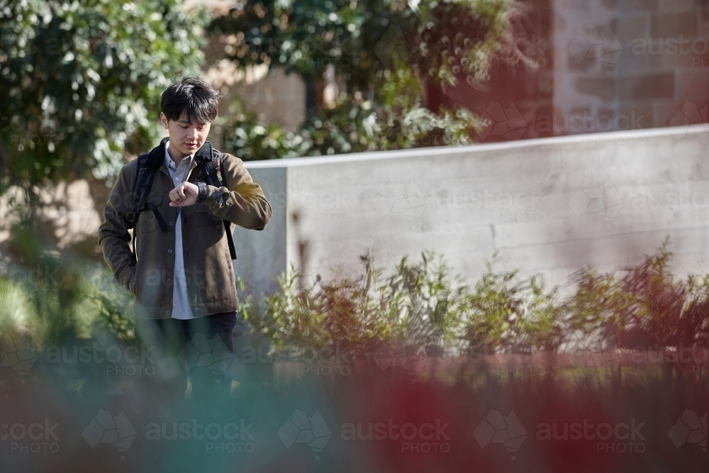 Young Asian university student standing on-campus checking smart watch - Australian Stock Image