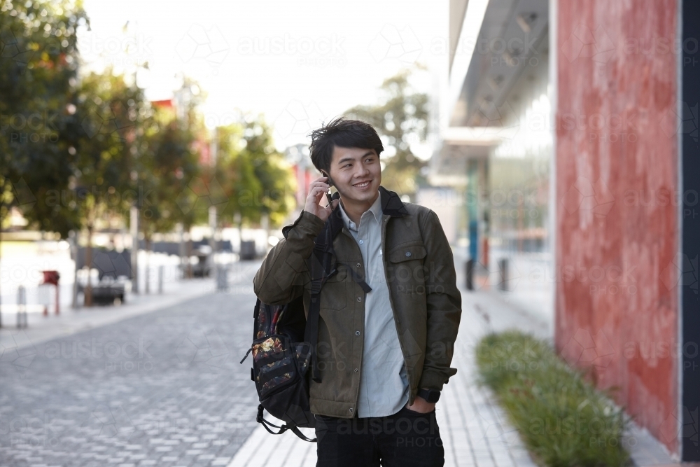 Young Asian university student walking to next to red wall class on-campus - Australian Stock Image