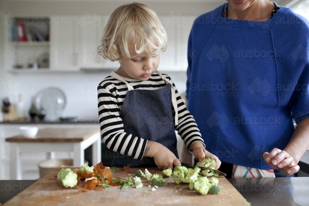 Young boy helping cook by cutting vegetables - Australian Stock Image