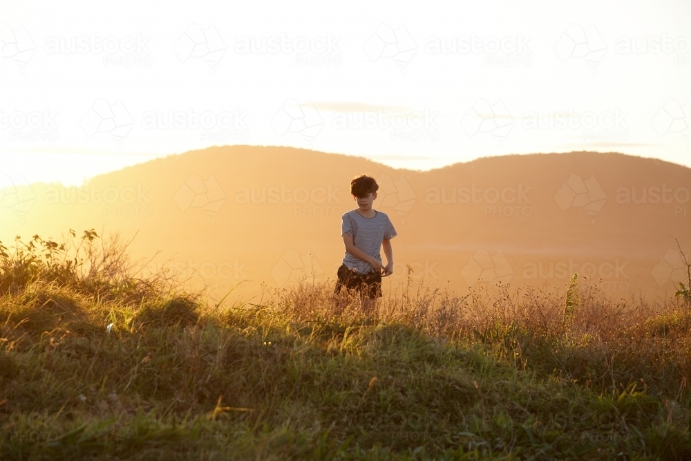 Young boy looking out to mountains at sunset - Australian Stock Image