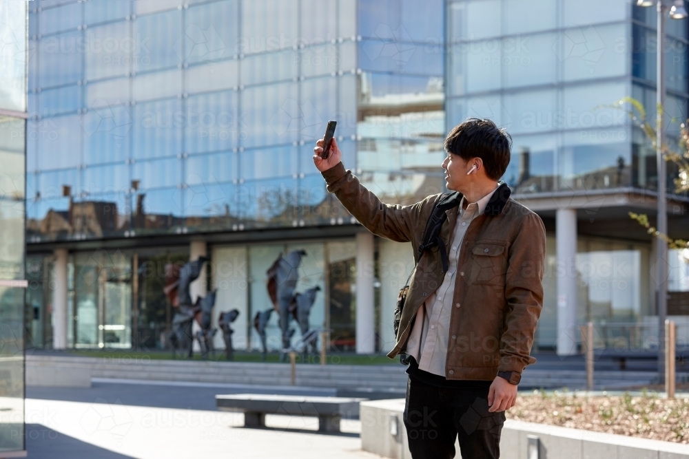 Young Chinese university student standing taking a photo with mobile phone - Australian Stock Image