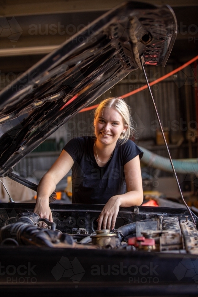 young female australian tradesperson mechanic working on car engine in auto repair garage - Australian Stock Image