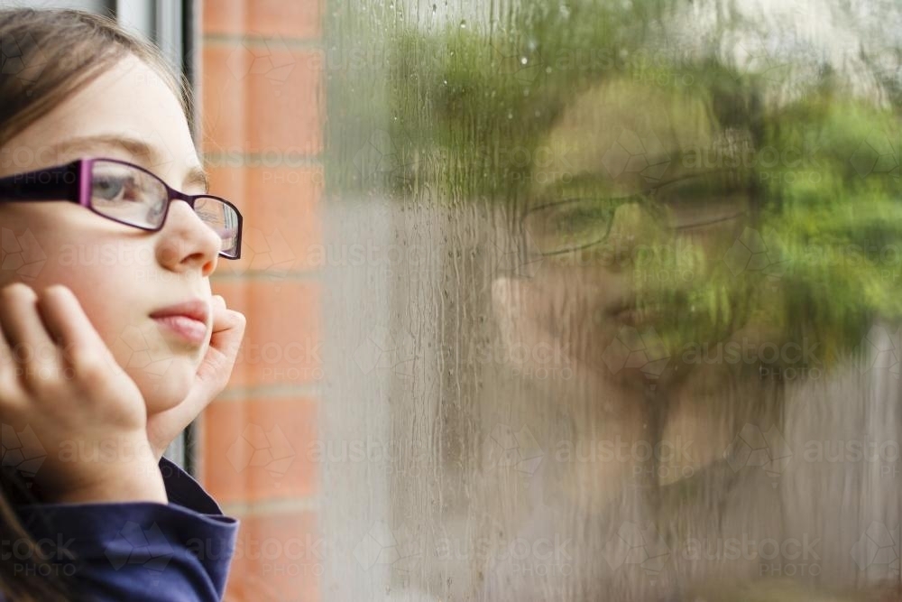 Young girl's face reflected in rainy window - Australian Stock Image