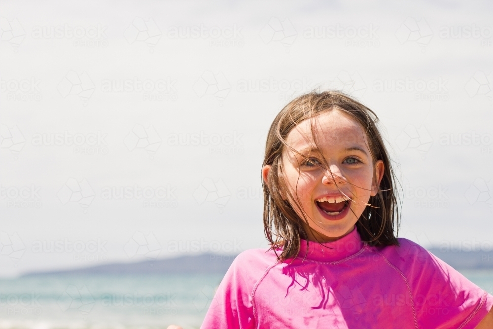 Young girl smiling in pink rash vest at the beach - Australian Stock Image