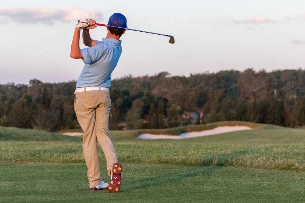 Young male golfer watching approach shot from behind - Australian Stock Image