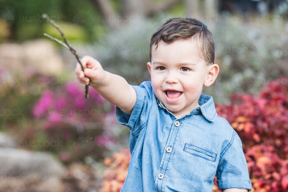 Young mixed race aboriginal caucasian boy playing with stick in garden - Australian Stock Image