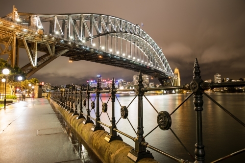 Wrought Iron fence along Sydney Harbour leading to The Sydney Harbour Bridge at night after the rain