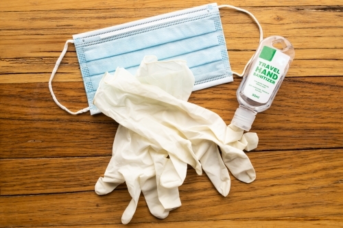 A blue disposable mask, cream disposable latex gloves and travel sized hand sanitizer