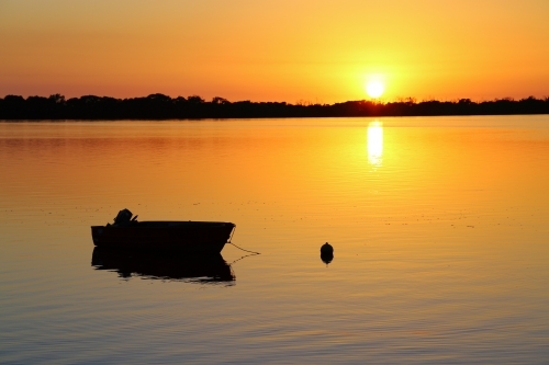 A calm golden sunrise over silhouetted dinghy on Pumicestone Passage