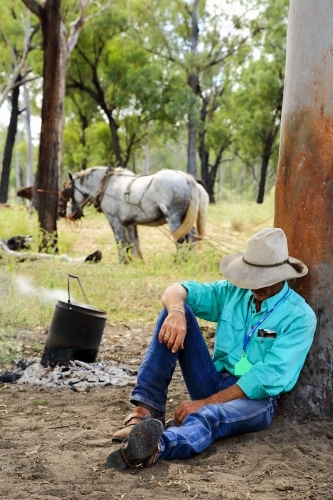 A cattle drover in his forties naps against a tree at morning tea.
