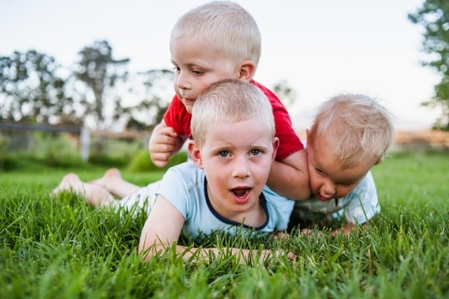 A close up of three brothers tackling each other in play on vibrant green grass.