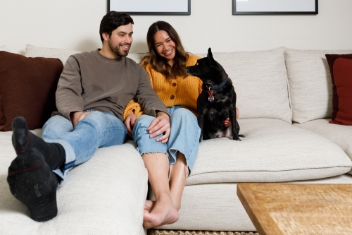 A couple at home on a couch looking at their dog