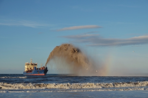 A dredging ship rainbowing sand into the ocean