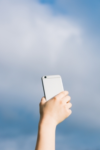 A female holding mobile phone against blue sky background.