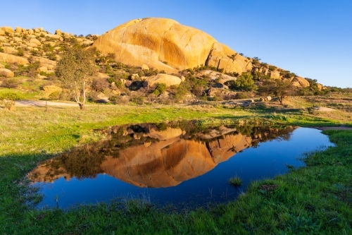 A large granite mountain in late evening light reflected in a dam