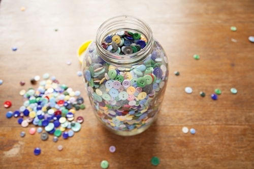 A Large jar of buttons sitting on a wooden table