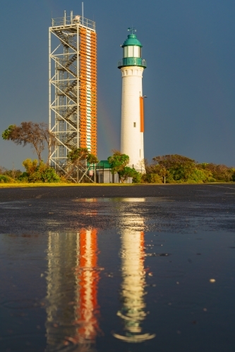 A light and signal tower highlighted against a dark sky and reflected in a puddle