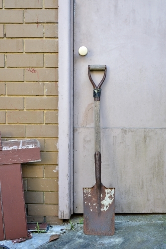 A rusty old spade leaning against a garage door